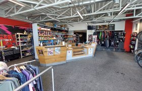 Innenansicht eines Fahrradgesch&auml;fts mit Werkstattbereich, Verkaufstresen und Fahrradzubeh&ouml;r.