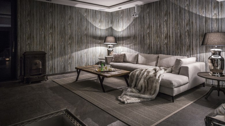 Gemütlicher Raum mit grauem Sofa, Holztisch, Kamin und Holzvertäfelung.