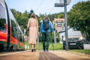 Zwei Personen am Bahnsteig, links der Zug und rechts ein Shuttlebus