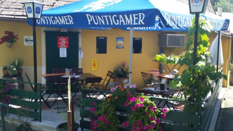 Außenbereich eines Wirtshauses mit blauen Sonnenschirmen und Blumen.