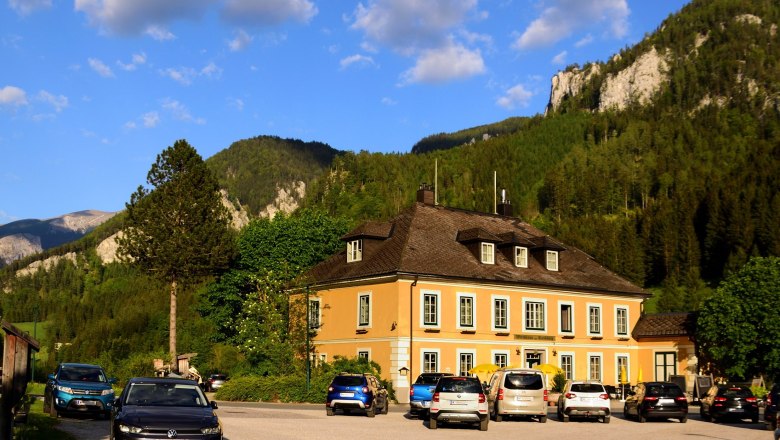 Wirtshaus zum Raxkönig, © Reinhard Maurer Ein gelbes Gebäude vor einer Bergkulisse mit geparkten Autos davor.