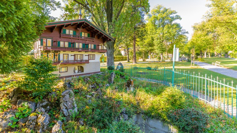 Miniaturhaus in einem Park mit Bäumen und einem Weg.