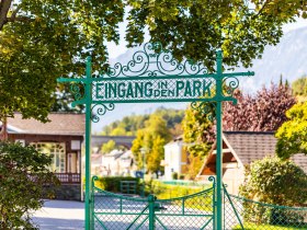 Grünes Tor mit Aufschrift "Eingang in den Park", im Hintergrund ist der Pavillon und die Rax zu sehen.