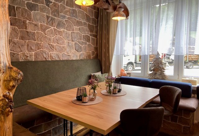 Gemütliche Sitzecke in einem Hofladen mit Holztisch, gepolsterten Stühlen und Dekorationen auf dem Tisch.