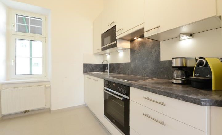 Moderne K&uuml;che mit wei&szlig;en Schr&auml;nken, grauer Arbeitsplatte, Ofen, Mikrowelle und Kaffeemaschinen.