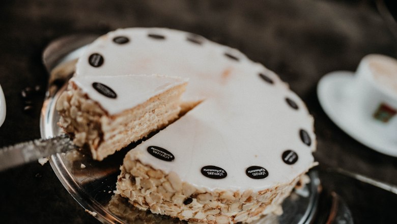 Eine angeschnittene Torte mit Mandeln und Schokoladendekoration auf einem Tablett.