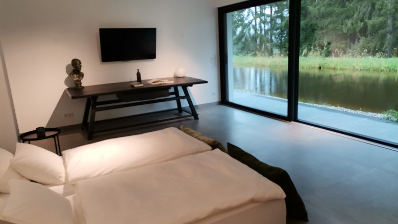 Modernes Schlafzimmer mit großem Fenster und Blick auf einen Teich.