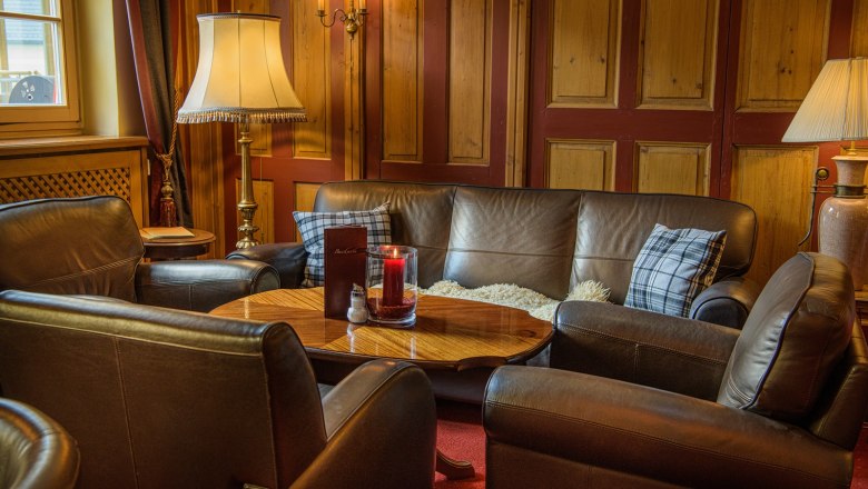 Gemütlicher Barbereich mit Ledersofas, Holztisch und Lampen.