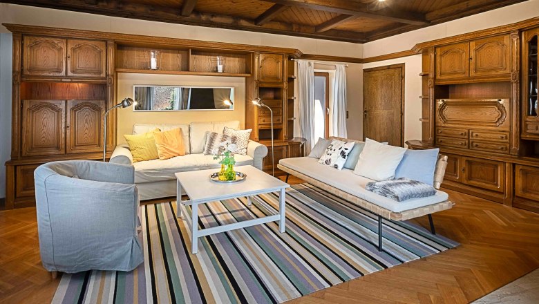 Gemütliches Wohnzimmer mit Holzmöbeln, Sofas, Teppich und Couchtisch.