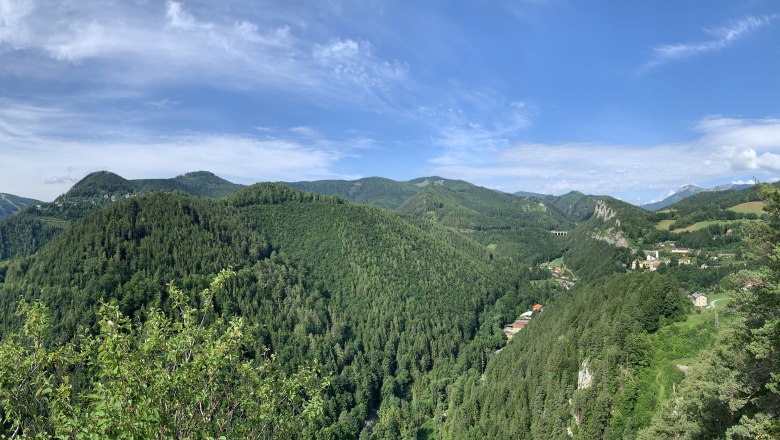 Panoramablick auf bewaldete Hügel und ein Tal mit verstreuten Häusern unter blauem Himmel.