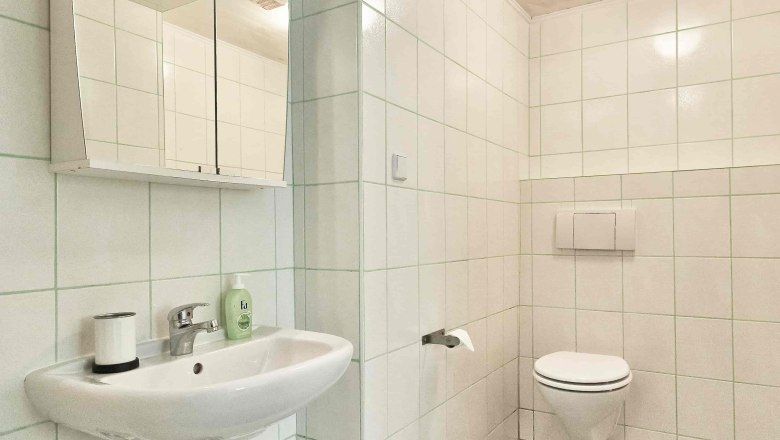 Modernes Badezimmer mit weißen Fliesen, Waschbecken, Spiegel und Toilette.