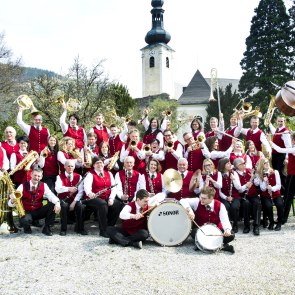 Eine Musikkapelle mit roter Uniform und den Musikinstrumenten vor einem Schloss