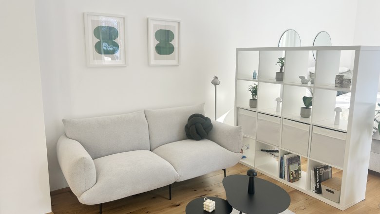 Modern eingerichtetes Wohnzimmer mit grauem Sofa, wei&szlig;en Regalen und zwei schwarzen Couchtischen.