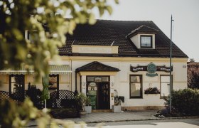 Traditionelles Gasthaus mit Schildern und Pflanzen im Vordergrund.