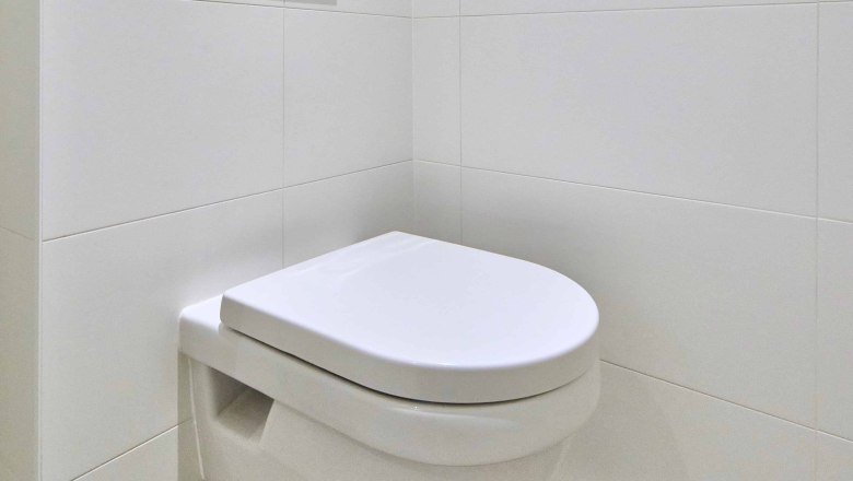 Modernes, weiß gefliestes Badezimmer mit wandhängender Toilette und Spülkasten.