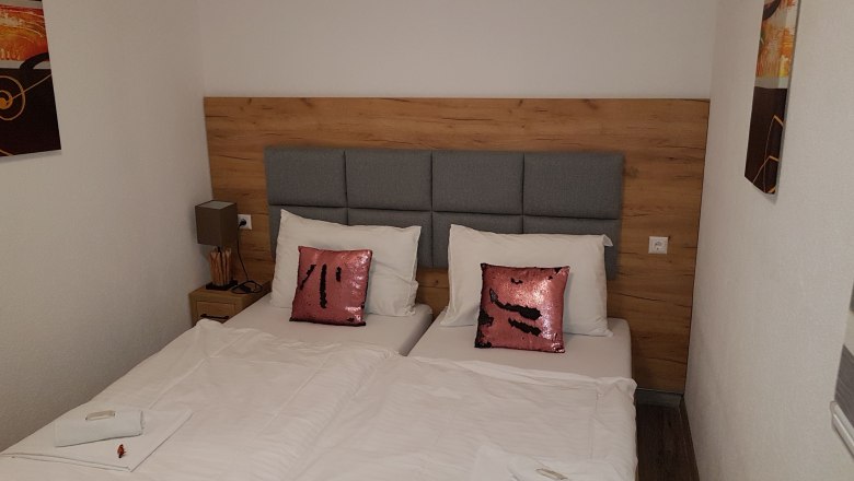 Doppelzimmer mit zwei Einzelbetten, grauem Kopfteil, rosa Pailletten-Kissen und weißer Bettwäsche.