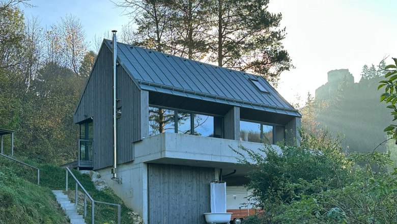Modernes Haus mit Holzfassade und großen Fenstern in bewaldeter Umgebung.