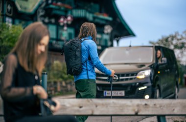 Ein Wanderer und eine Frau, im Hintergrund ein schwarzer Schuttlebus. 