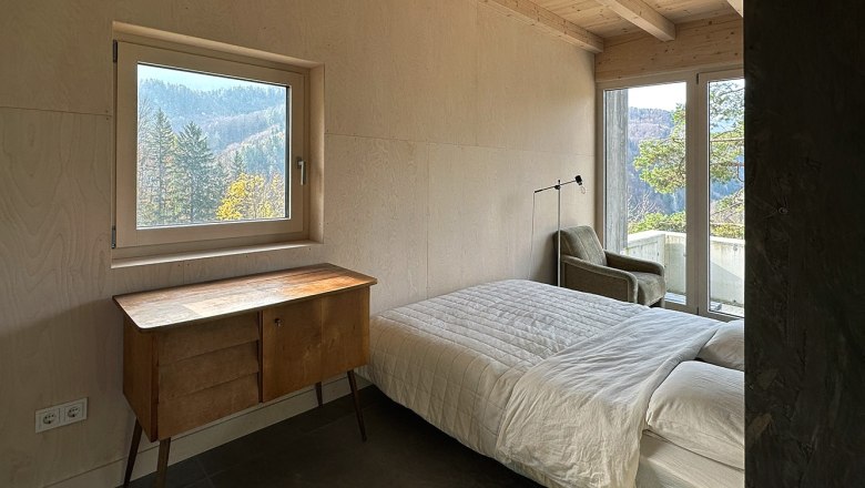 Schlafzimmer mit Bett, Holzdecke, Fenster mit Bergblick und Kommode.