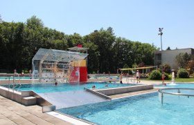 Freibad mit Kletterwand, umgeben von Bäumen.