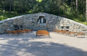 Steingrotte mit Marienstatue und Bänken davor im Freien.