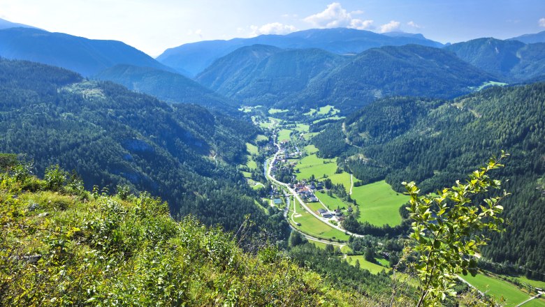 Panoramablick auf ein grünes Tal mit Bergen im Hintergrund.