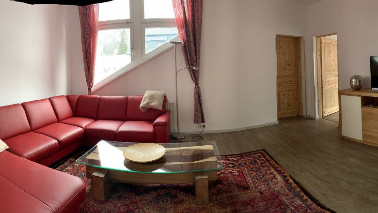 Wohnzimmer mit rotem Ledersofa, Glastisch, Teppich und TV auf Holzschrank.