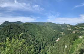 Panoramablick auf bewaldete Hügel und ein Tal mit verstreuten Häusern unter blauem Himmel.