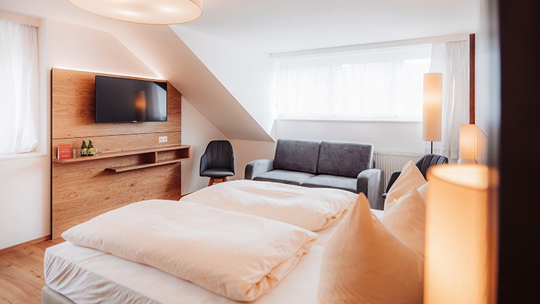 Modernes Hotelzimmer mit Doppelbett, Sofa, TV und stilvoller Beleuchtung.