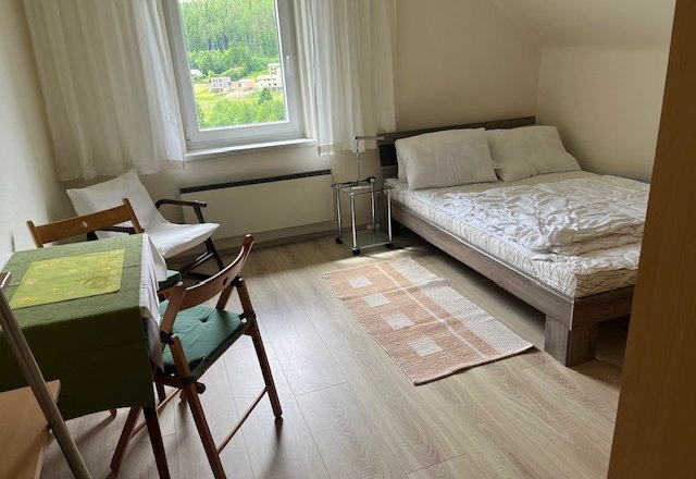 Helles Schlafzimmer mit Doppelbett, Tisch und Stühlen, Fenster mit Blick auf grüne Landschaft.