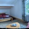 Gemütliches Schlafzimmer mit Holzbett, Sofa und großem Fenster mit Vorhängen.