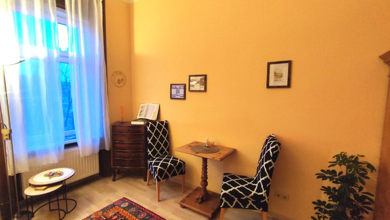 Gemütliches Zimmer mit zwei Stühlen, kleinem Tisch, Teppich und Pflanzen.