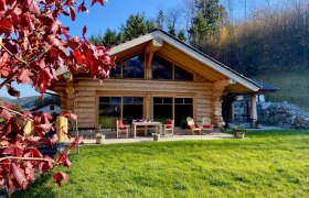 Holzchalet mit Terrasse und roten Herbstbl&auml;ttern im Vordergrund.