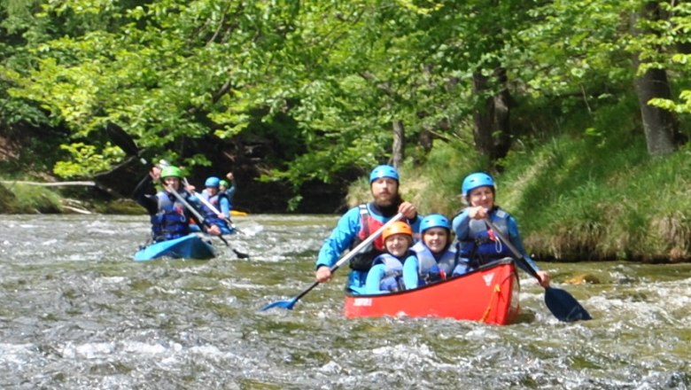 Menschen in Kanus paddeln auf einem Fluss in einer gr&uuml;nen Waldlandschaft.