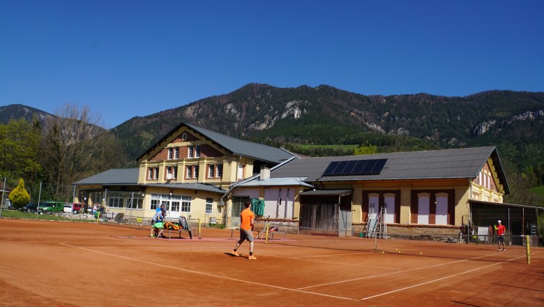 Tennisplatz vor einem Geb&auml;ude mit Bergen im Hintergrund.