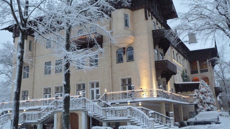 Winter Hotel Marienhof, © Hotel Marienhof Ein großes, elegantes Hotel im Winter, umgeben von schneebedeckten Bäumen und einem verschneiten Auto.