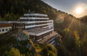 Ein Hotel auf einem Hügel bei Sonnenuntergang, umgeben von Wald.
