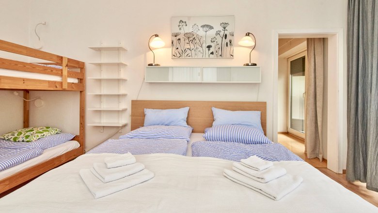 Schlafzimmer mit Doppelbett, Etagenbett, blauer Bettwäsche und Handtüchern.