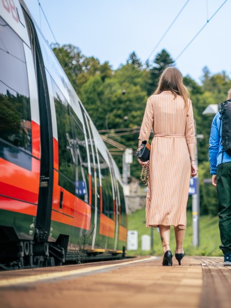 Zwei Personen am Bahnsteig, links der Zug und rechts ein Shuttlebus