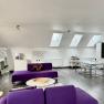 Modernes Loft mit violetten Sofas, Esstisch und K&uuml;chenzeile unter Dachfenstern.