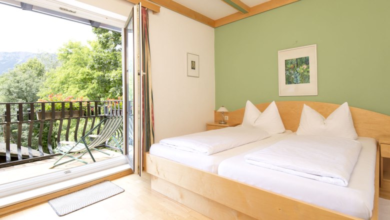 Doppelzimmer mit hellen Holzbetten in der Mitte und grünem Wänden mit Blick auf den Balkon