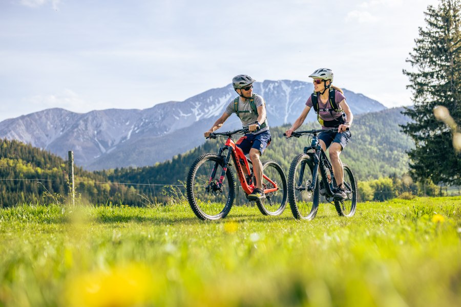 Zwei Mountainbiker auf dem Rad in grüner Landschaft, hinterhalb Berglandschaft