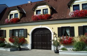 Gelbes Haus mit roten Blumen und braunem Dach.
