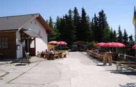 Außenbereich der Pollereshütte mit Sitzplätzen und Sonnenschirmen.