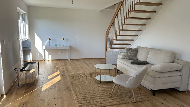 Modernes Wohnzimmer mit Holztreppe, Sofa, Sessel und Couchtisch auf Holzboden.