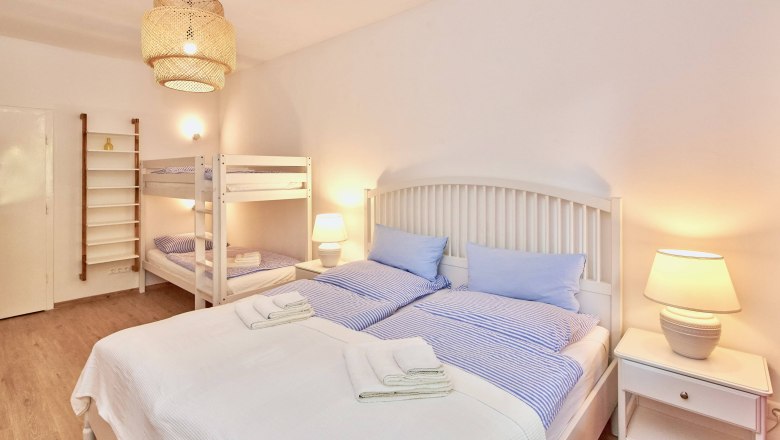 Schlafzimmer mit Doppelbett, Etagenbett, Nachttischlampen und heller Einrichtung.
