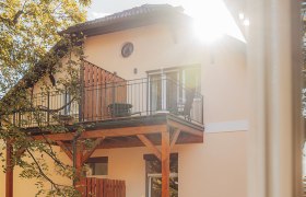 Haus mit Balkon und Sonnenschein durch Bäume.