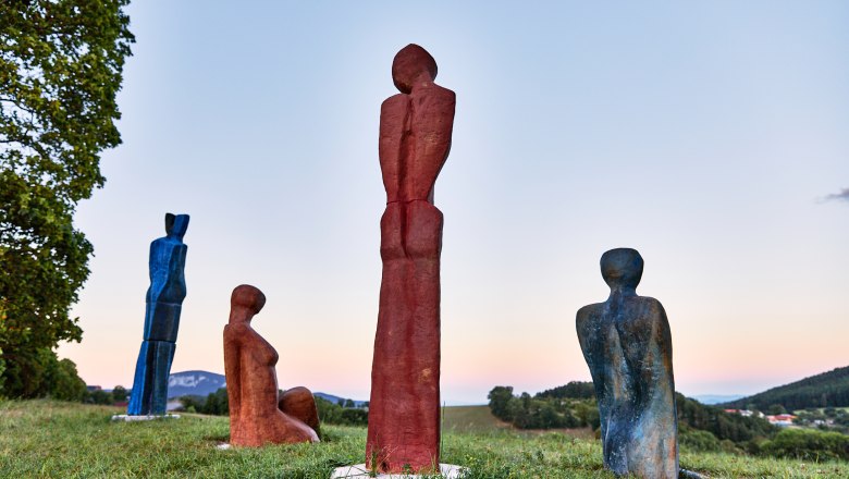 Vier bunte Skulpturen auf einer Wiese bei Sonnenuntergang.