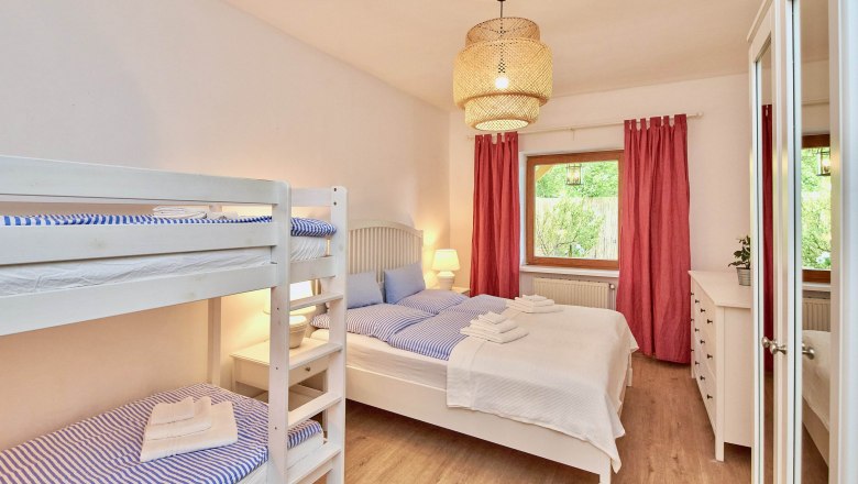 Schlafzimmer mit Etagenbett, Doppelbett, rotem Vorhang und Holzfußboden.