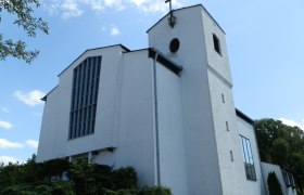 Wei&szlig;e Kirche mit Turm und Kreuz vor blauem Himmel.